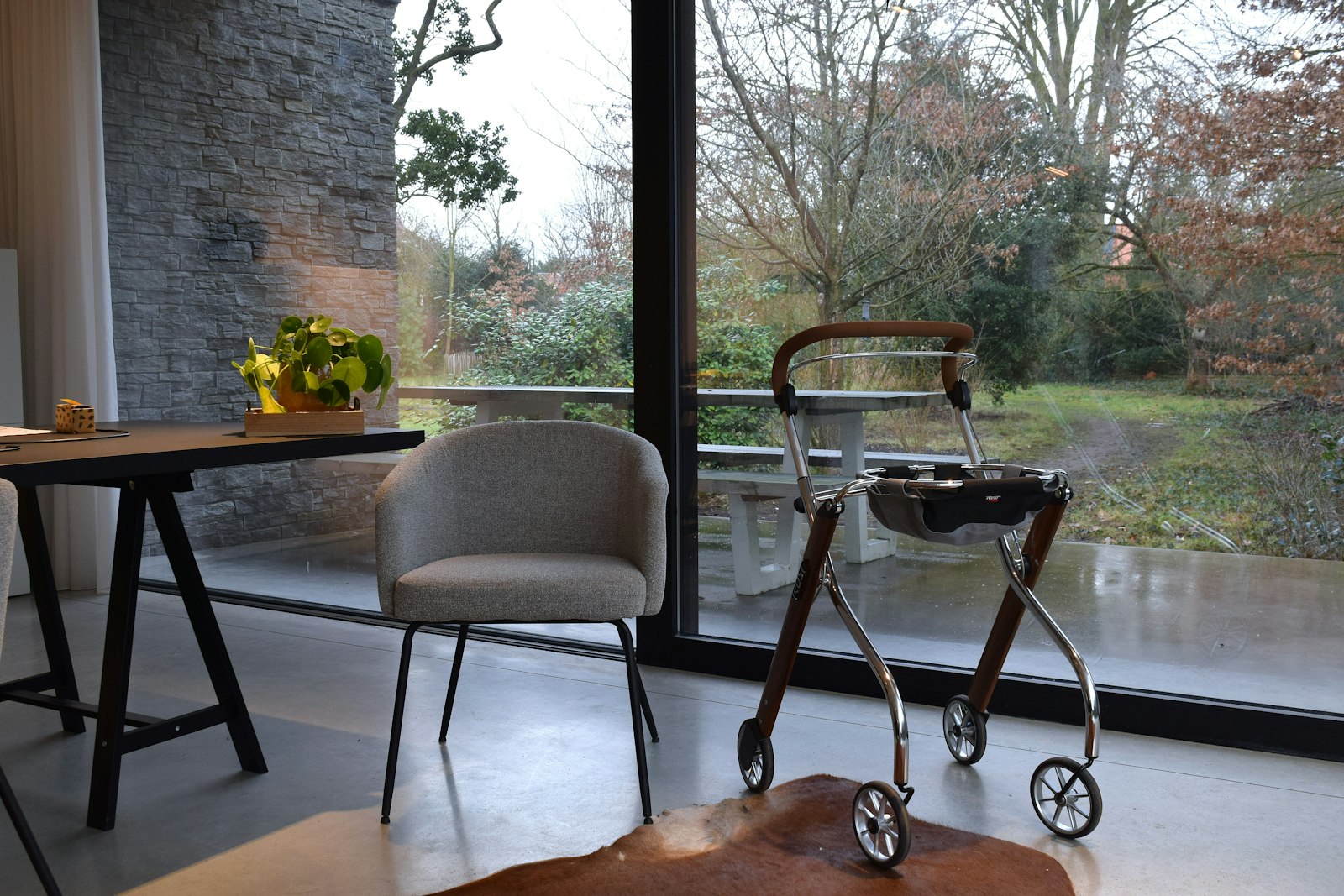Walking aid and chair beside a large window overlooking a garden